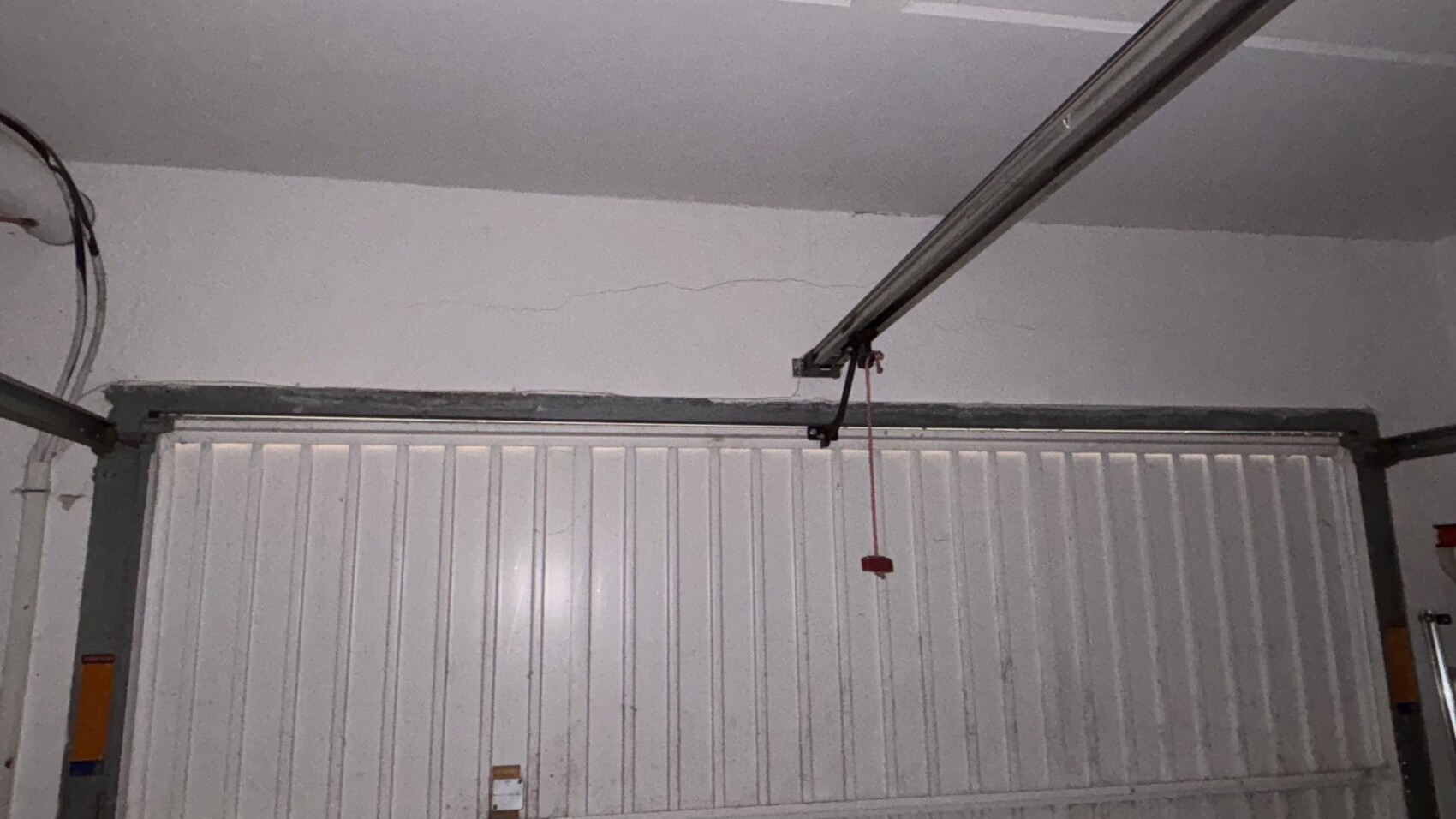 Weißes Garagentor mit vertikalen Paneelen; rote Zugschnur hängt von der Decke herab.