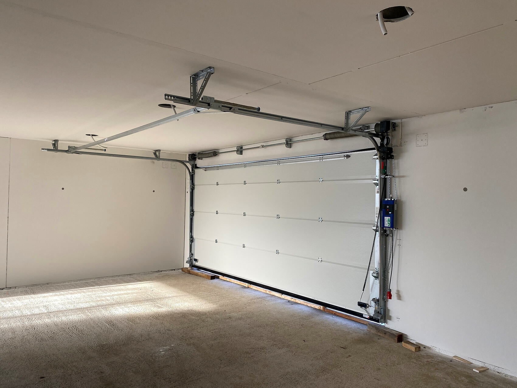 Helle Garage mit geschlossenem Sektionaltor, Torantrieb, Führungsschienen und Steuerbox.