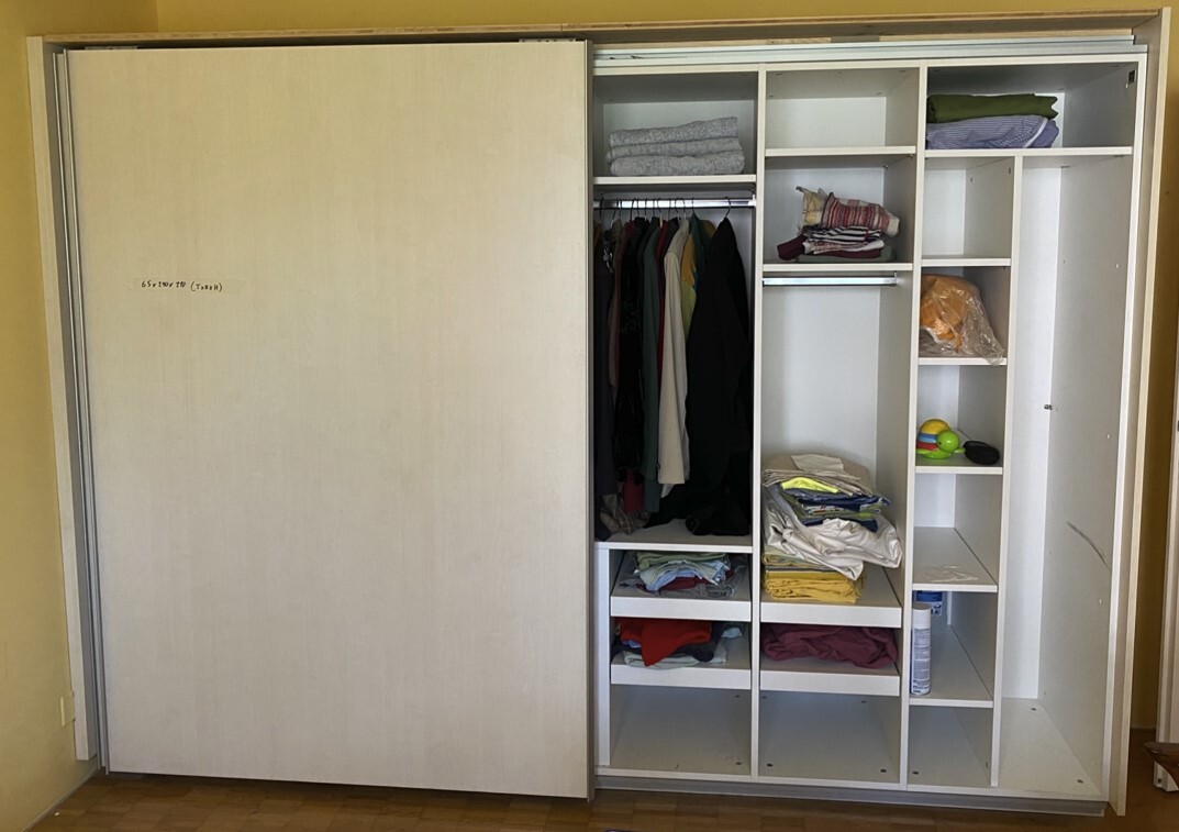 Offene Kleiderschrankseite mit Kleiderstange, gefalteten Textilien und Spielzeug.