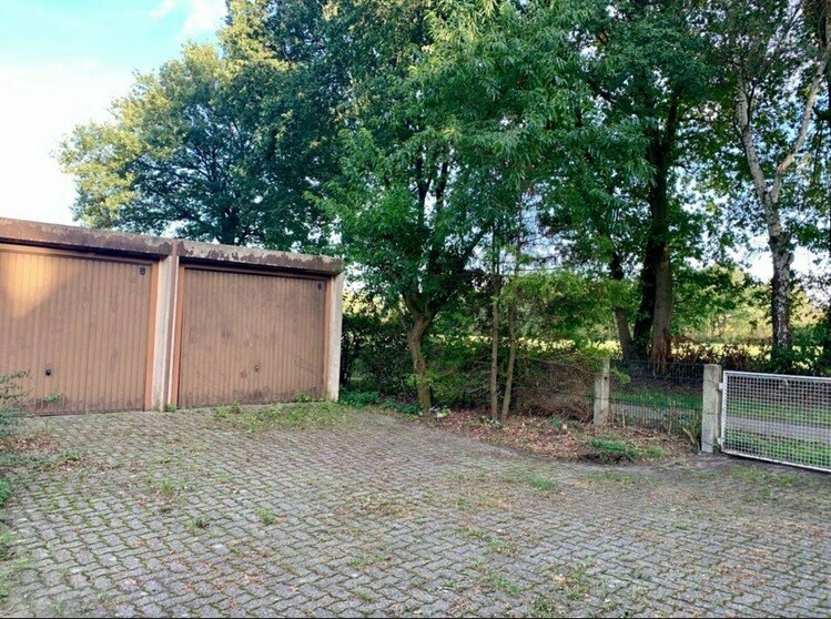 Gepflasterte Hoffläche mit zwei braunen Garagen, Bäumen und Metallzauntor an der Seite.