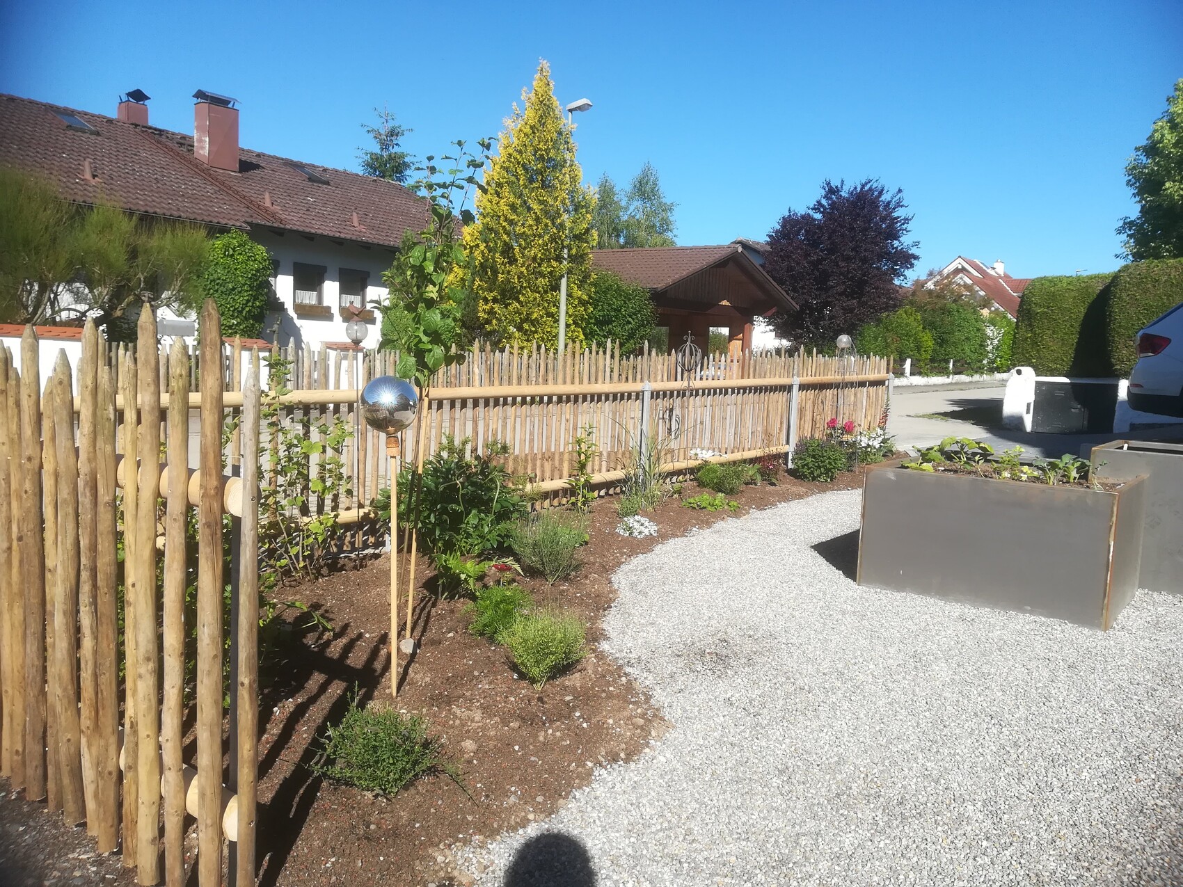 Garten mit Holzzaun, Kiesweg, Pflanzboxen und Haus im Hintergrund