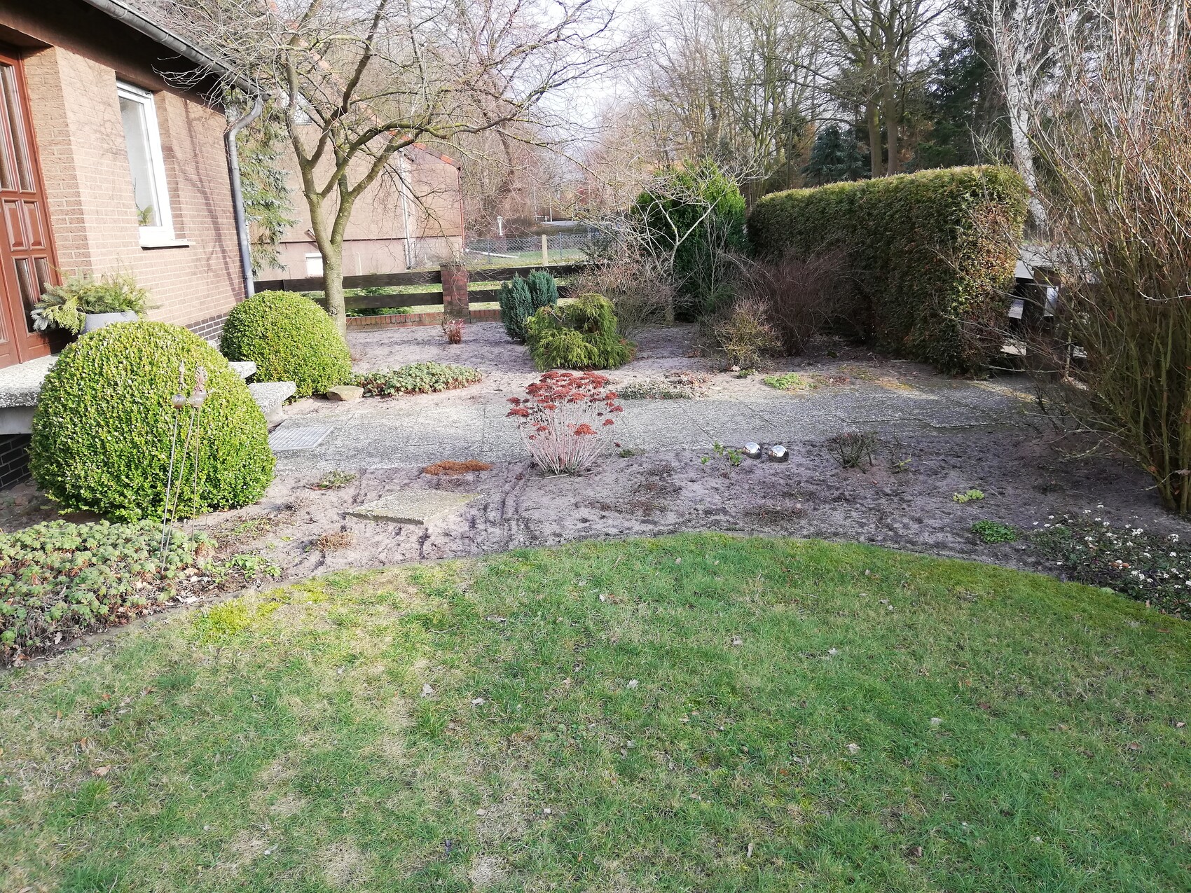 Vorderansicht eines Wohnhauses mit Garten, Buschhecken, Kiesflächen und Rasen.