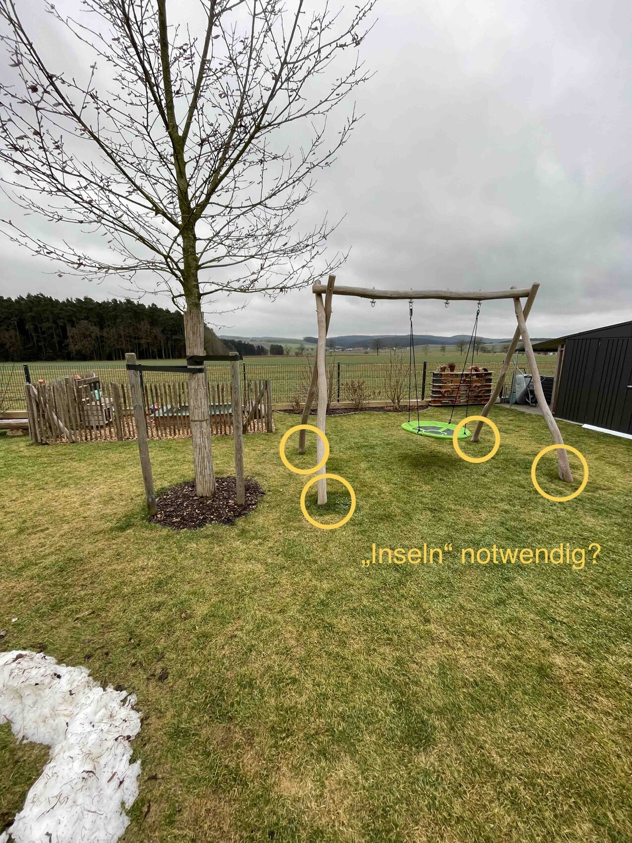 Holzschaukelgestell im Garten mit grünem Sitz, Baum, Zaun und ländlichem Hintergrund.
