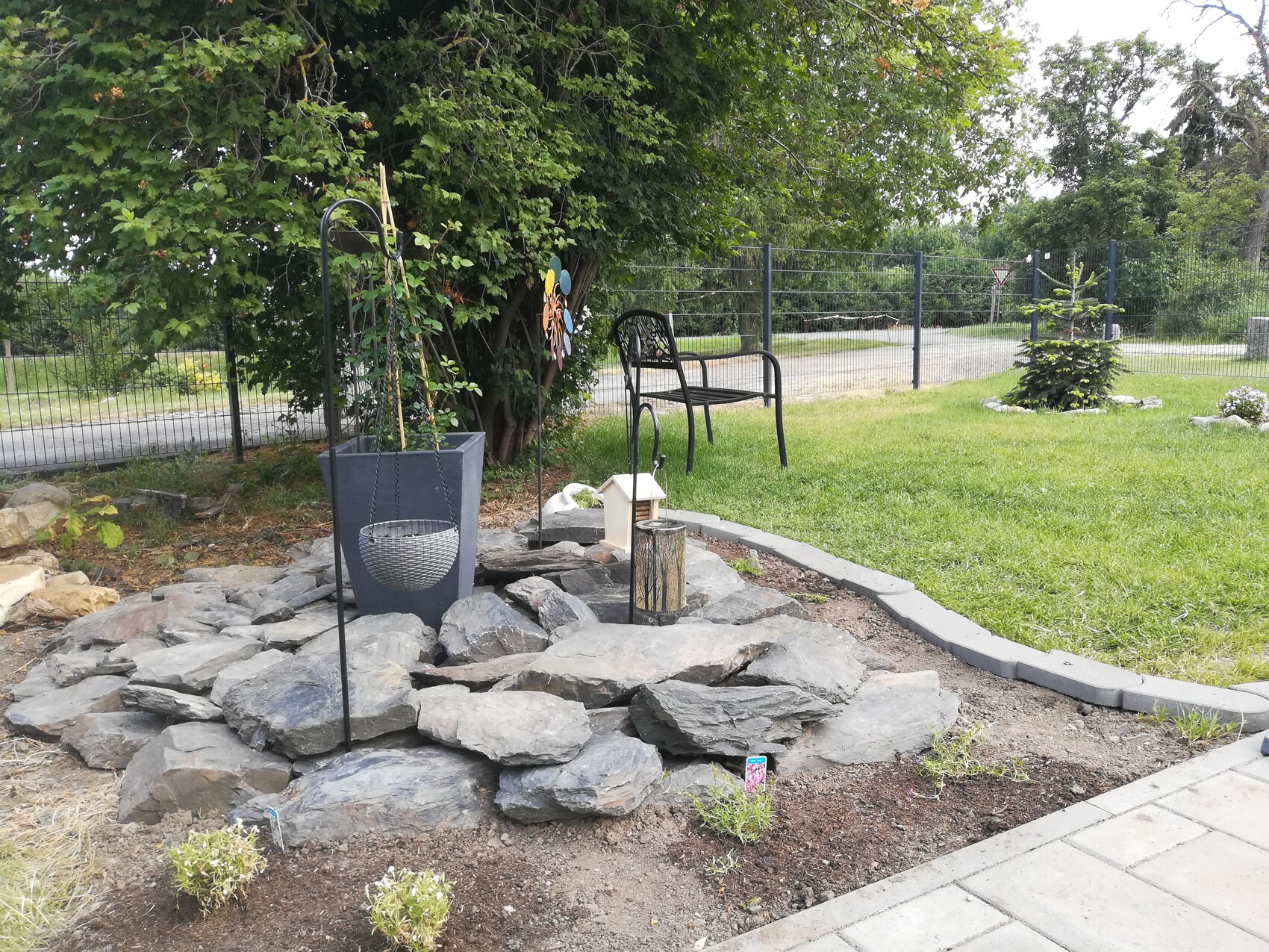 Garten mit Steinen, Hängekorb, Metallstuhl und Zaun im Hintergrund