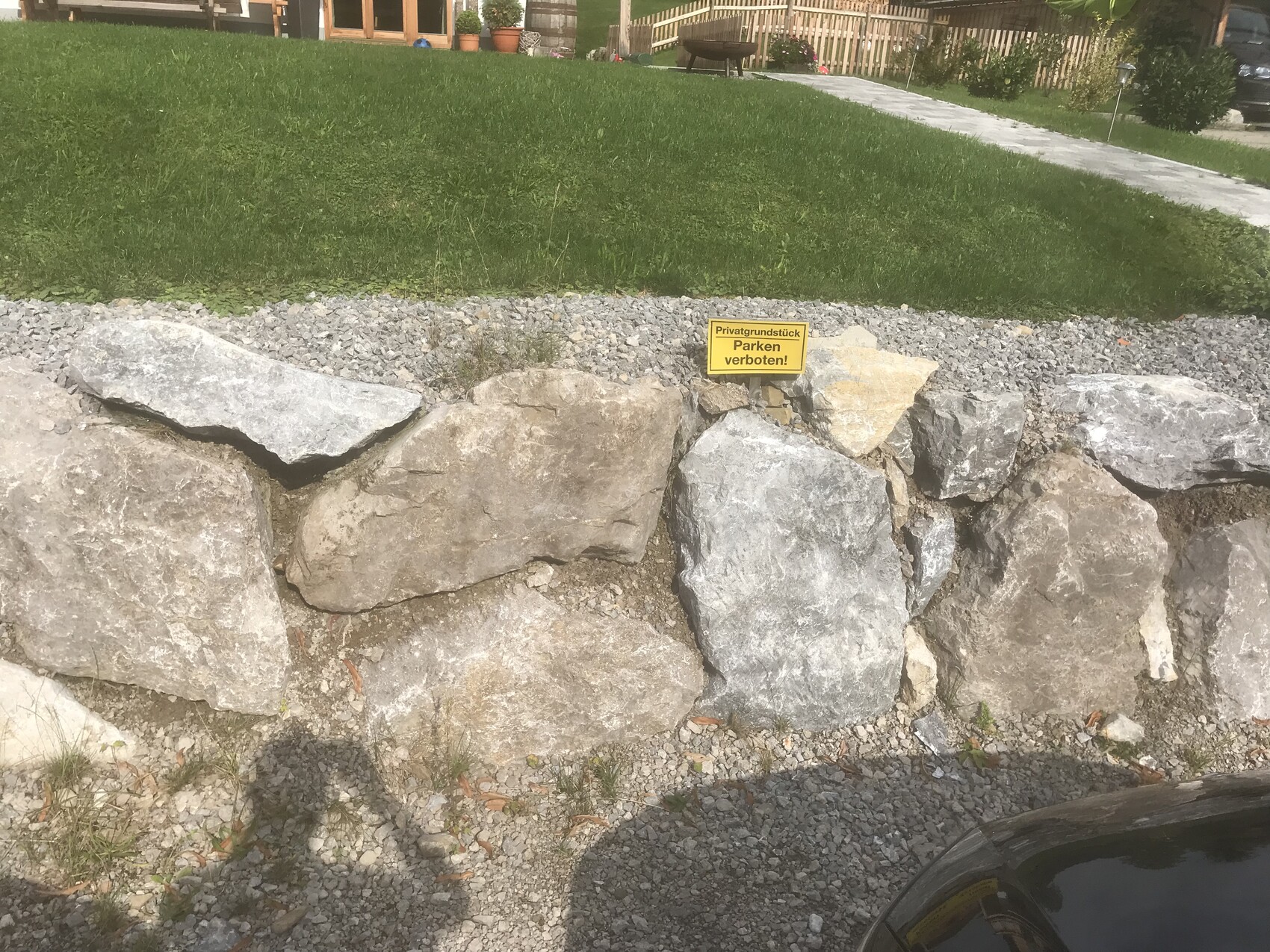 Große Steinmauer als Gartengrenze mit Grasfläche, Kiesweg und Parkverbot-Schild