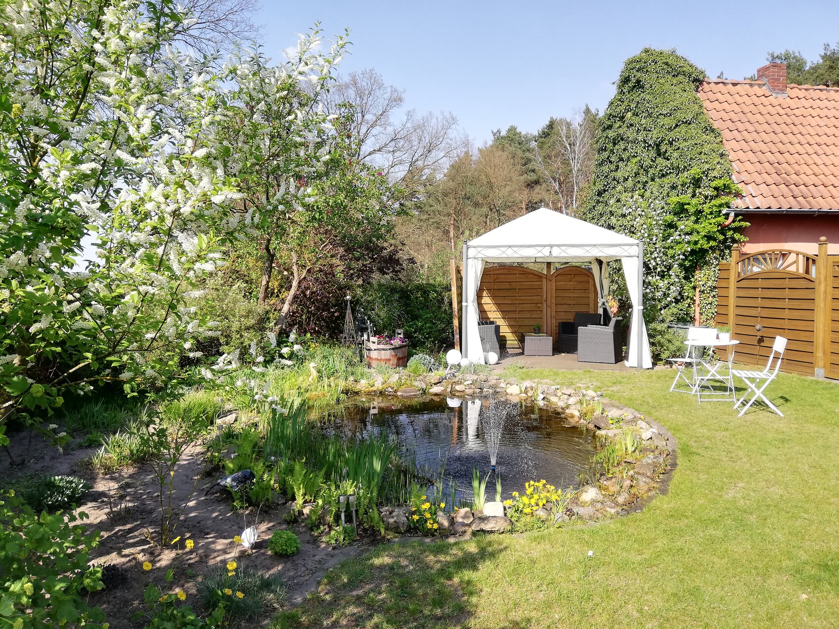 Garten mit Teich, weißem Pavillon und gemütlicher Sitzgruppe auf Rasen
