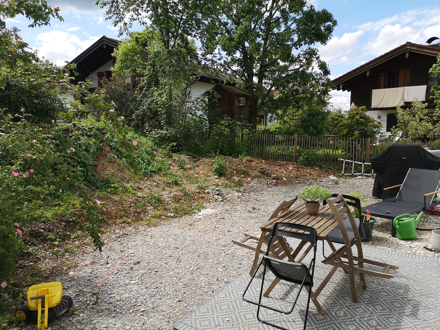 Garten im Hinterhof mit Holztisch, Stühlen, Grill, Pflanzen, Wäscheleine und Häuser.