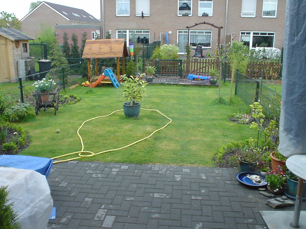Grüner Garten mit Spielturm, Rutsche, Terrasse und Zäunen im Hintergrund