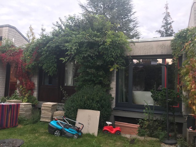 Gartenbereich vor einem Haus mit Terrasse, rankende Pflanzen und Spielzeugfahrzeuge