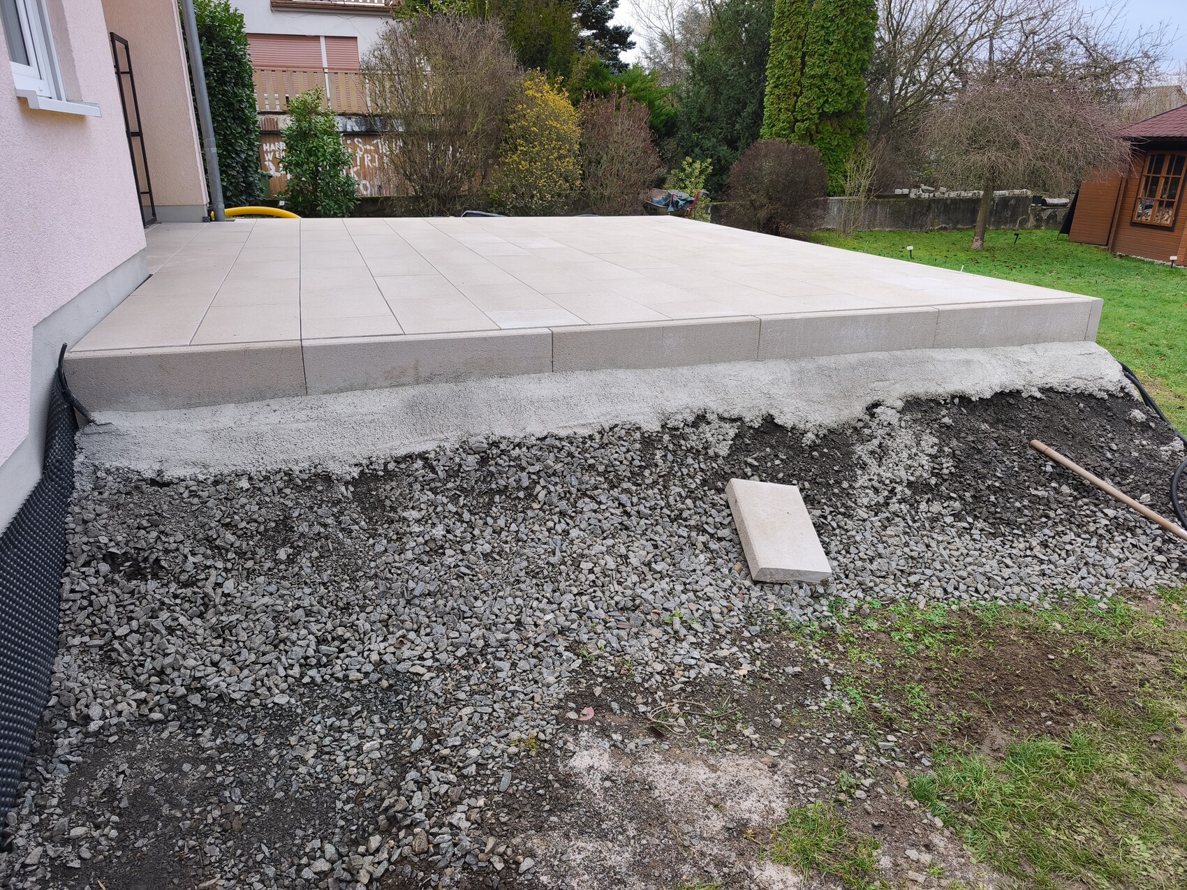 Neue Terrasse mit großen Terrassenplatten auf Kies-Unterbau neben dem Haus