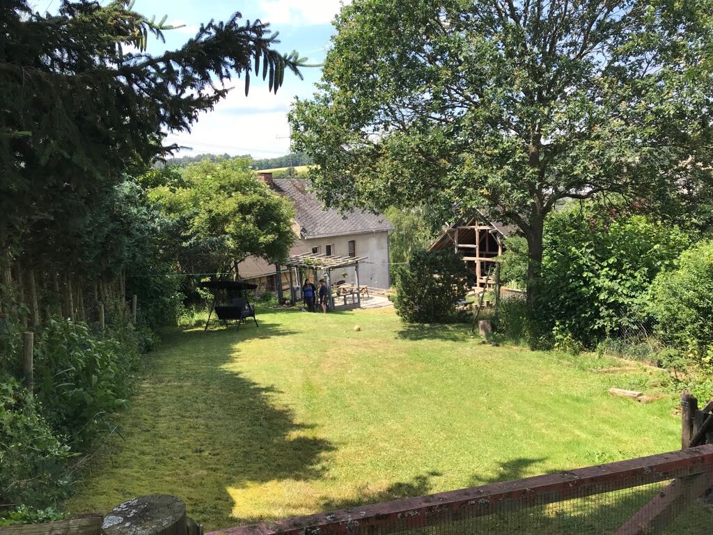 Garten mit Rasen, Bäumen und einer Holzkonstruktion neben einem Haus im Hintergrund