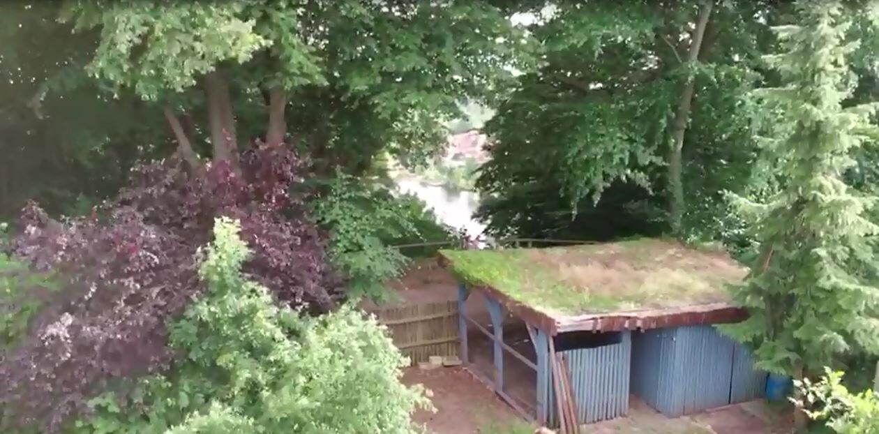 Kleiner Gartenschuppen mit Grasdach im Garten, von Bäumen umgeben