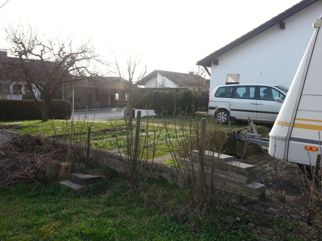 Gartenbereich mit Stufen, Sträuchern, Wohnwagen und Wohnmobil neben einem Haus.