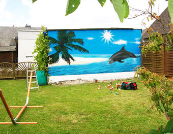 Hinterhof mit blauer Wandmalerei Strand-Delfin-Palmen und grünem Rasen