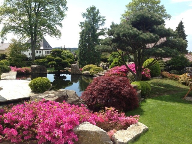 Gartenanlage mit Teich, Steinbrücken, bunten Blumen und Bäumen