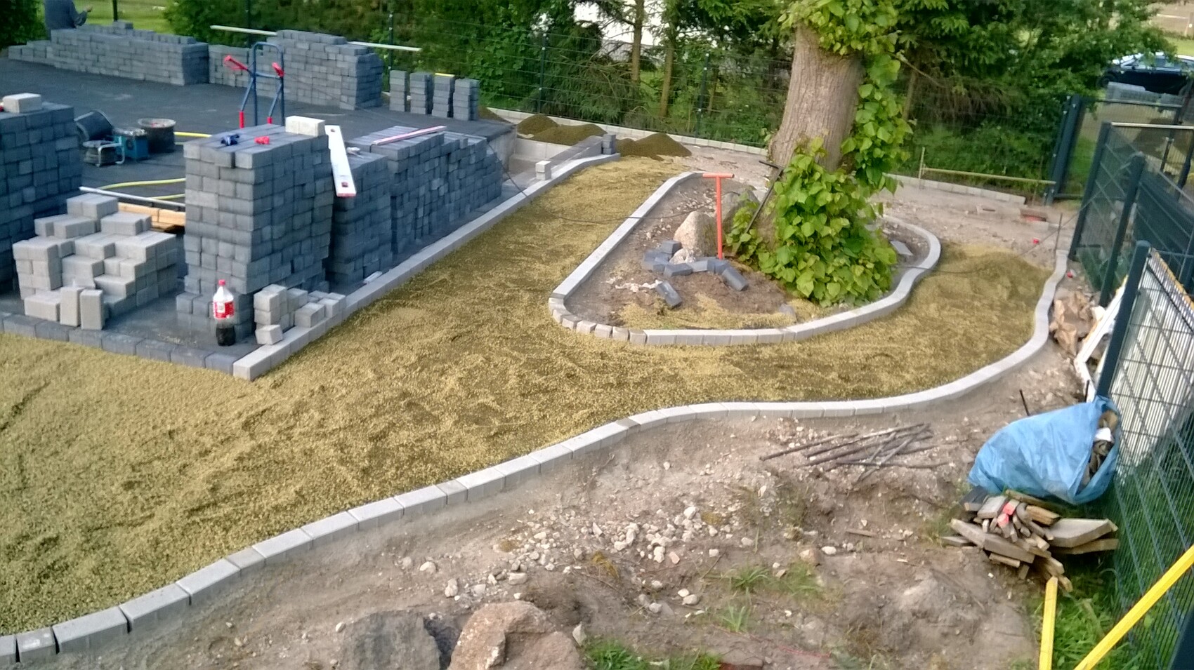 Gartenbaustelle: stapelweise graue Betonblöcke, Pflasterarbeiten um einen Baum.
