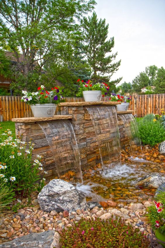 Gartenbrunnen aus Stein mit drei Wasserfällen, Blumentöpfe, Kiesbecken.