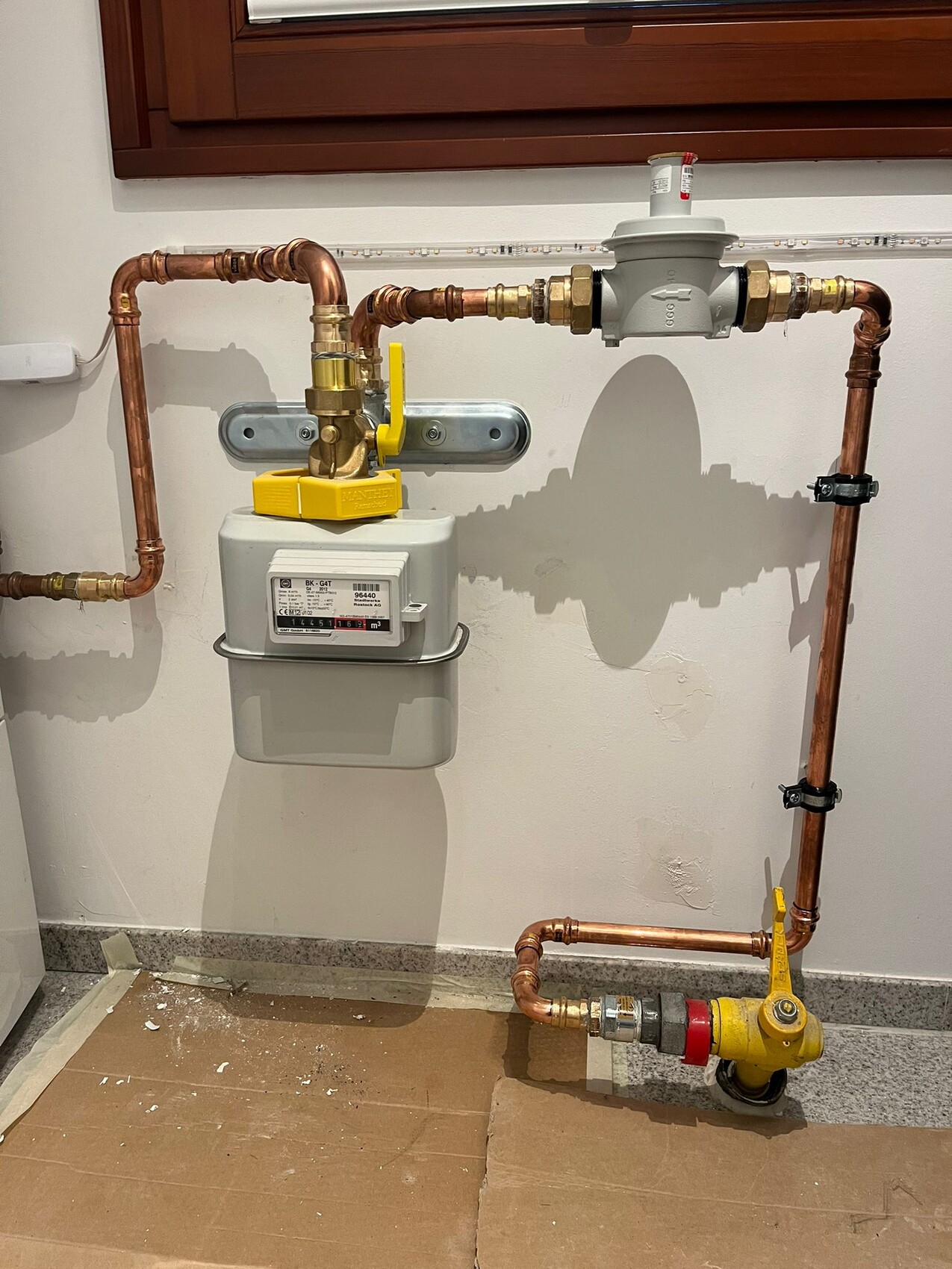 Gaszähler mit Hauptabsperrventil und Kupferleitungen an der Wand.