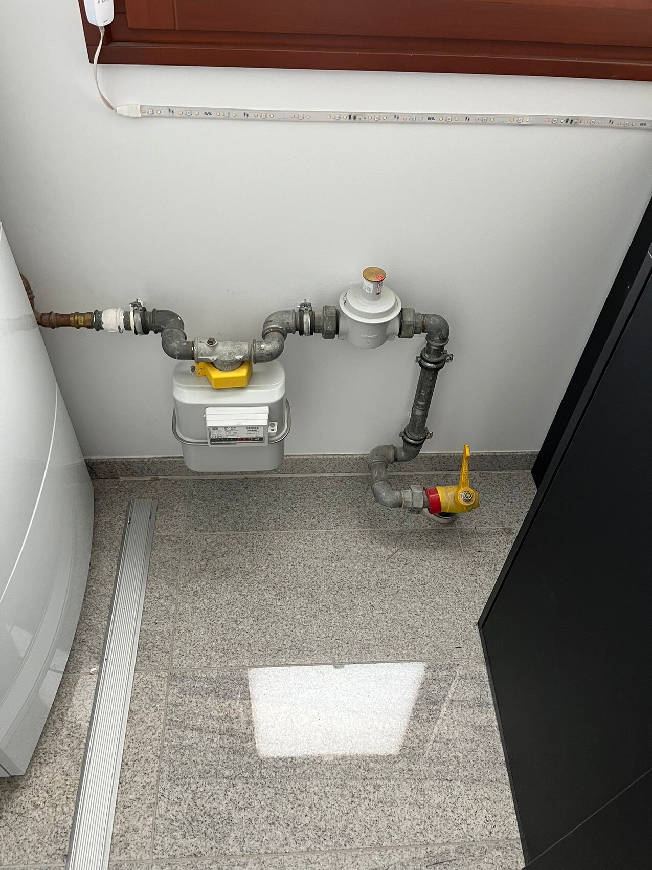 Gaszähler mit Rohren, Absperrhahn und Regler in einem Waschkeller.
