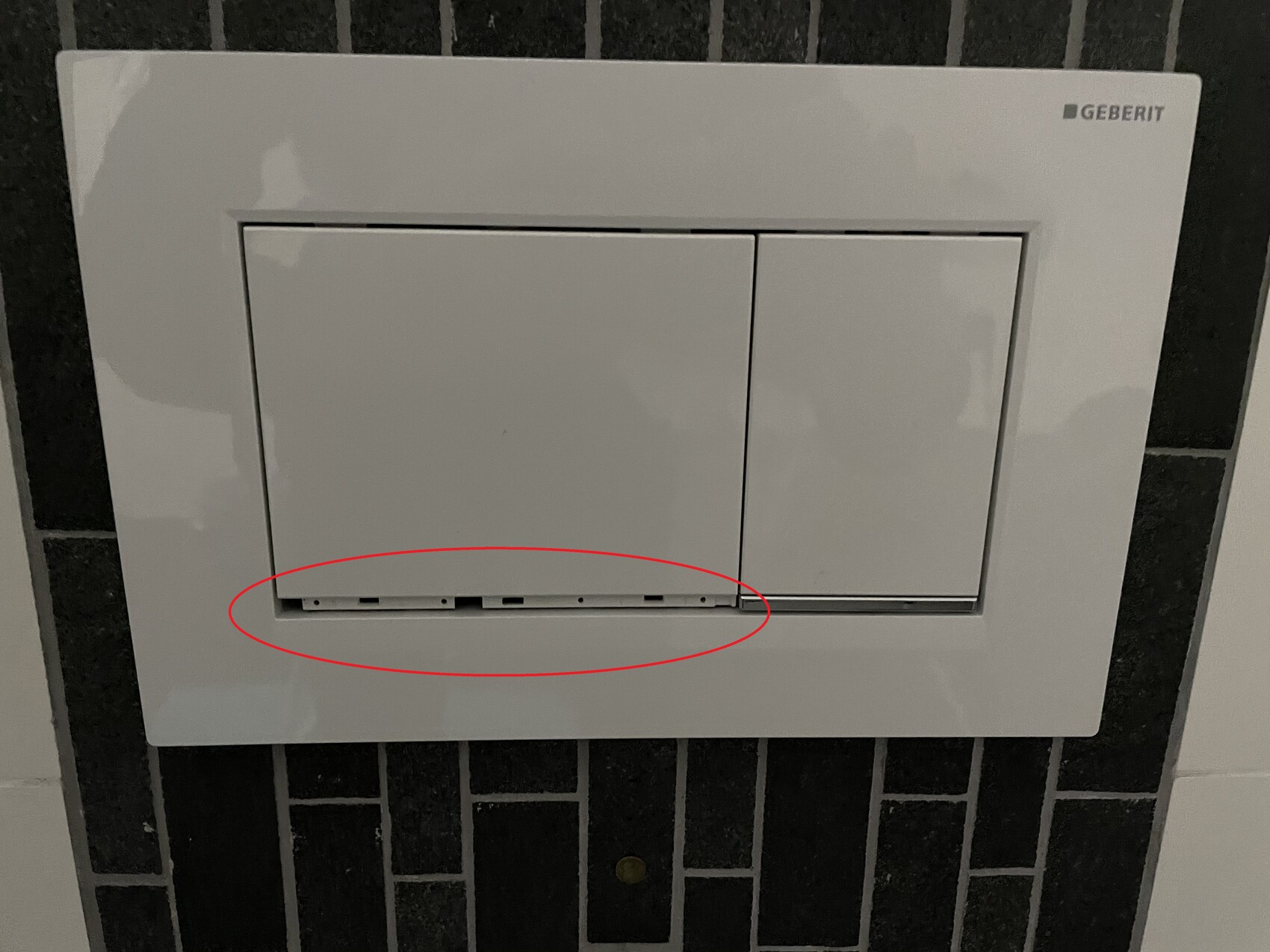 Weiße Geberit Spülplatte mit zwei Tasten an schwarzer Fliesenwand; untere Öffnungen sichtbar.