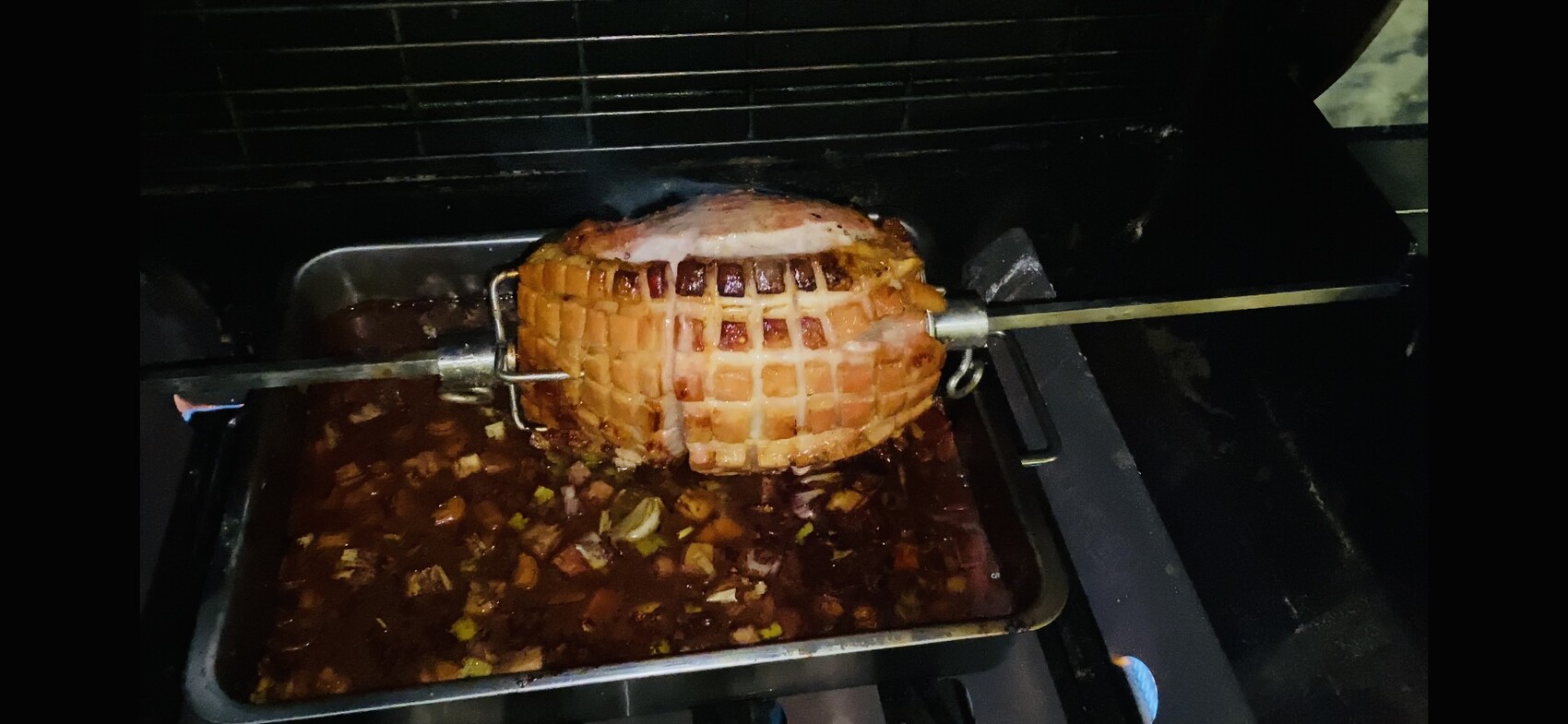 Rotierendes Fleisch am Spieß im Ofen, Bratensauce mit kleingeschnittenem Gemüse darunter