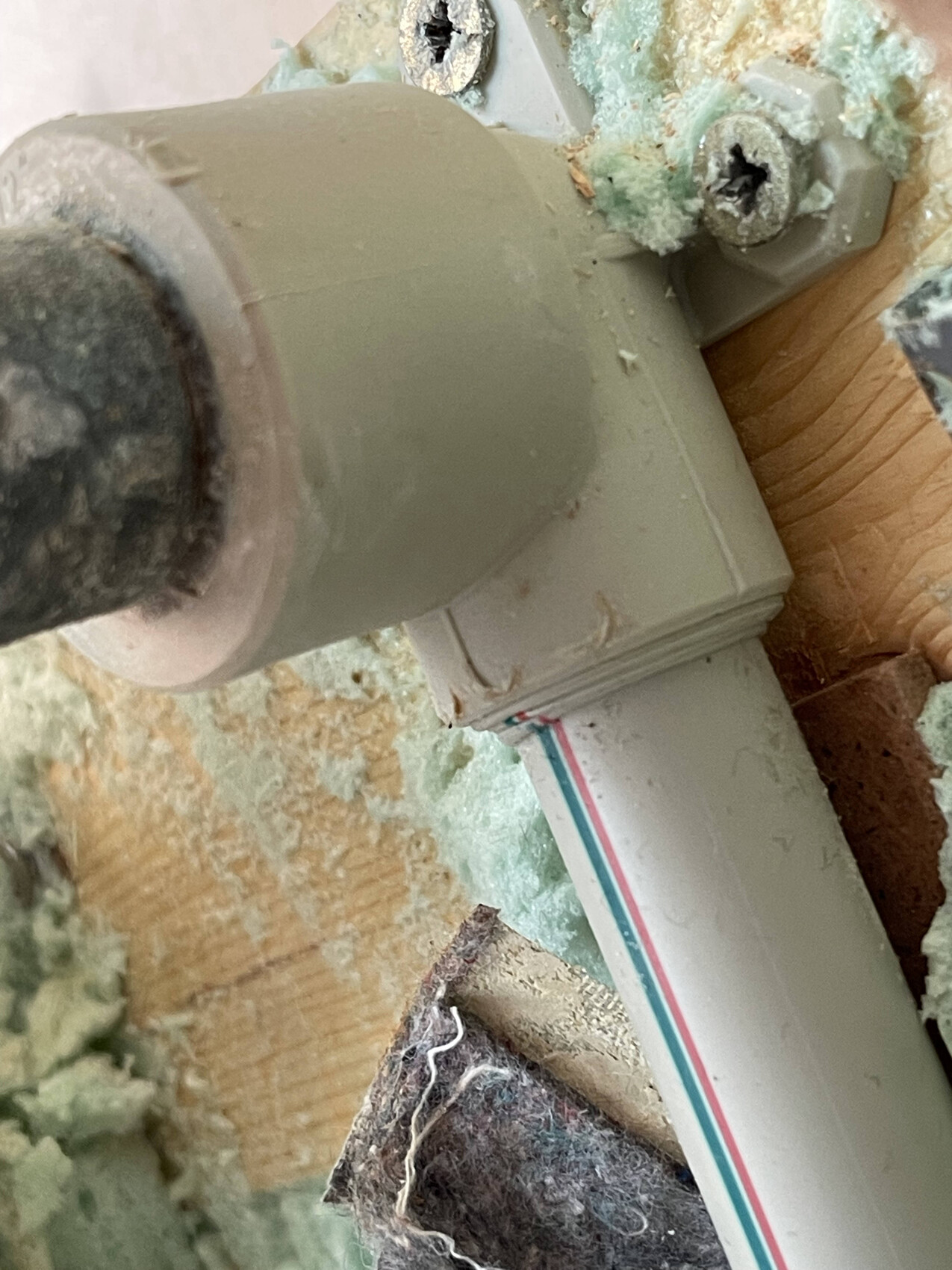 Nahaufnahme von grauem PVC-Rohr mit 90-Grad-Bogen, umgeben von Dämmung und Holz.