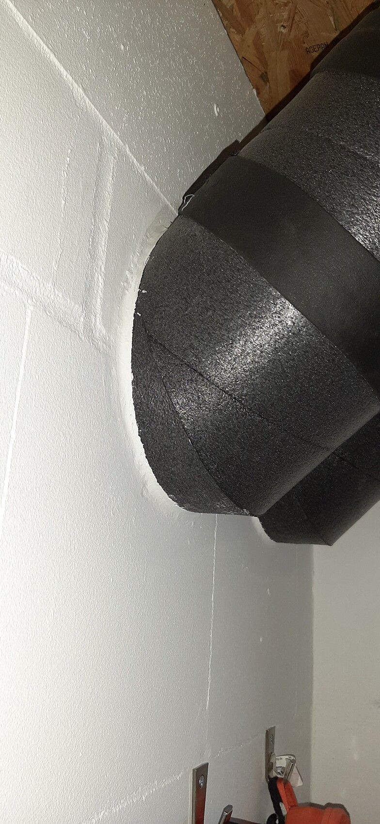 Großer, runder, schwarzer isolierter Luftkanal an einer weiß gestrichenen Wand, seitlich.