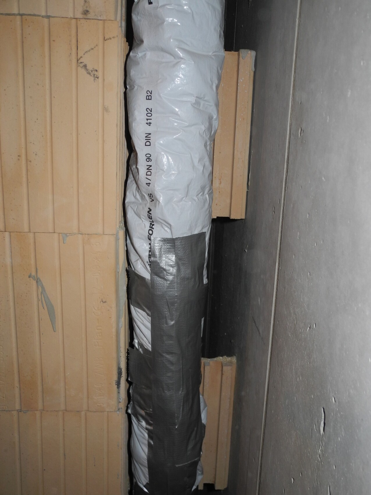 Gedämmtes Installationsrohr in einer Bauwand zwischen Holzlatten und Betonwand.