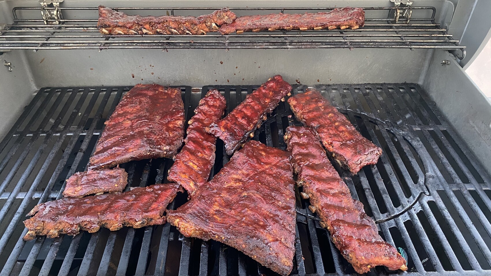 Grill mit rot-glasierten Rippchen auf Rost, mehrere Stücke liegen darauf.