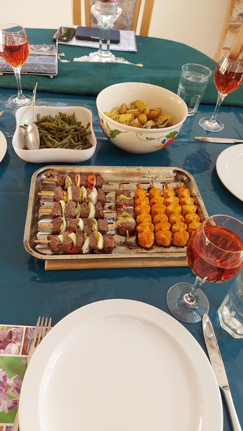 Grillspieße mit Fleisch und Zwiebeln; Kartoffeln; grüne Bohnen; Rotwein am Tisch.