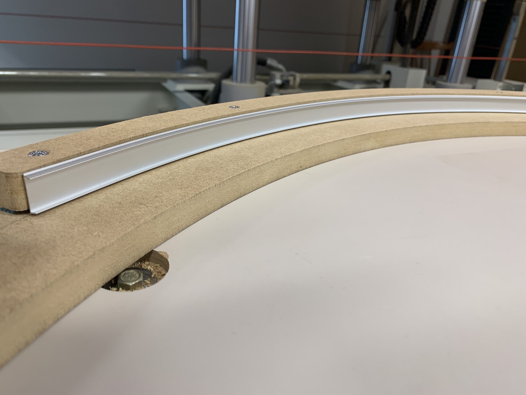 Nahaufnahme eines gebogenen Holzrahmens mit Metallführung auf weißer Tischplatte.