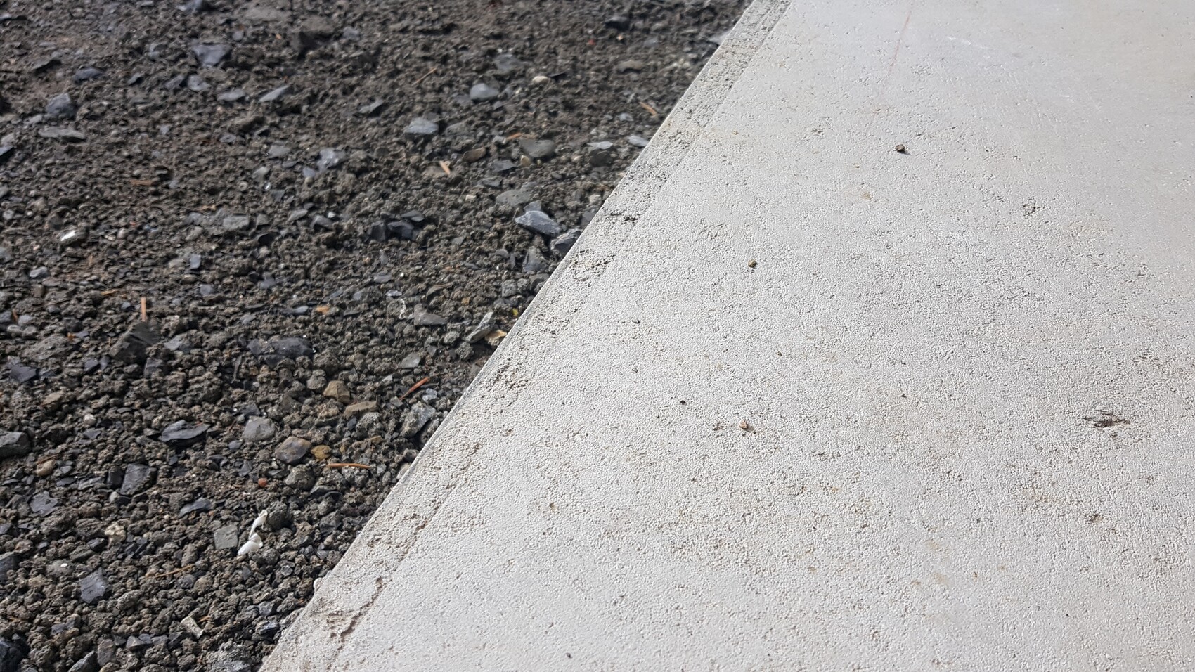 Kiesboden links und glatter Betonweg rechts, durch eine geschwungene Kante getrennt.