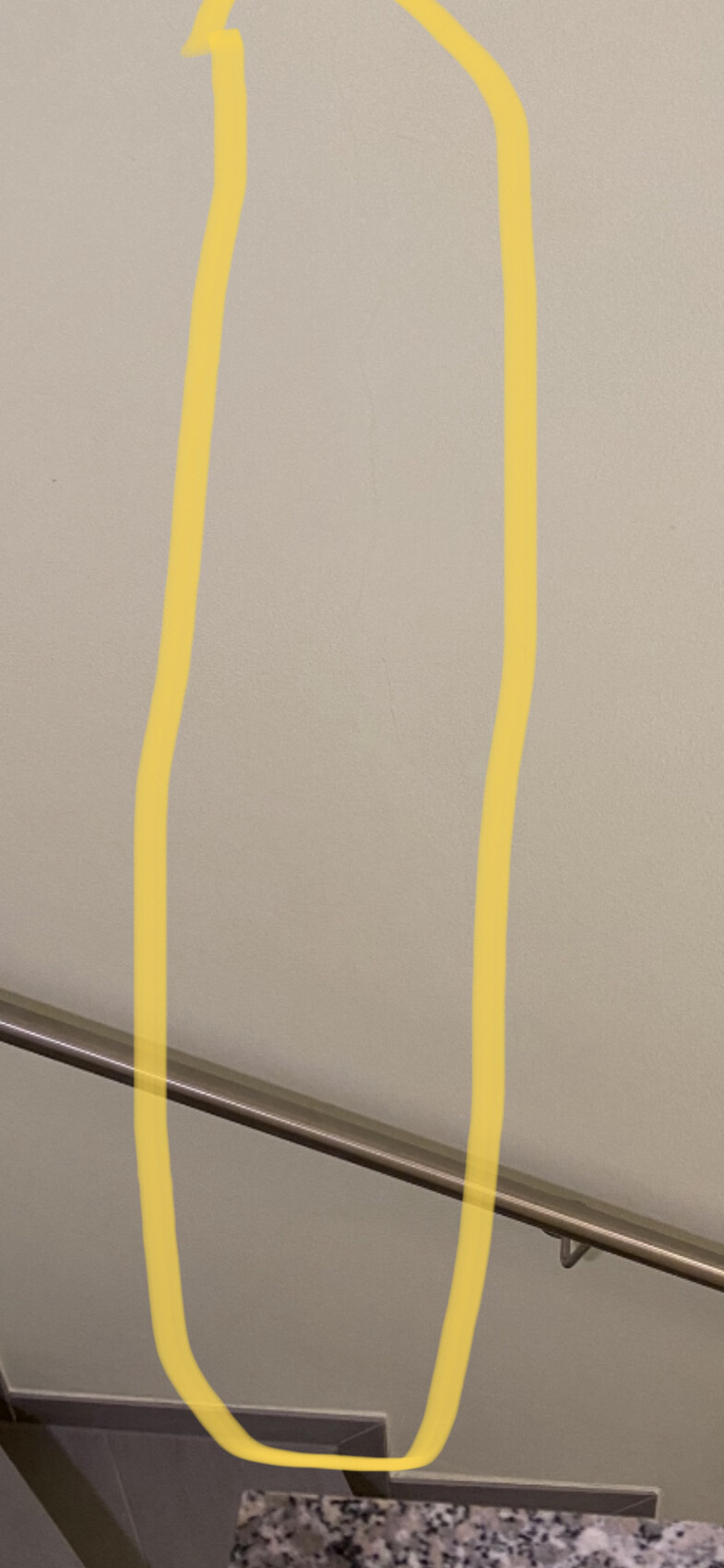 Beige Wand mit gelbem Umriss einer langen ovalen Form über einem Metallhandlauf.