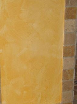 Aussenwand mit gelbem Putz neben Steinmauer