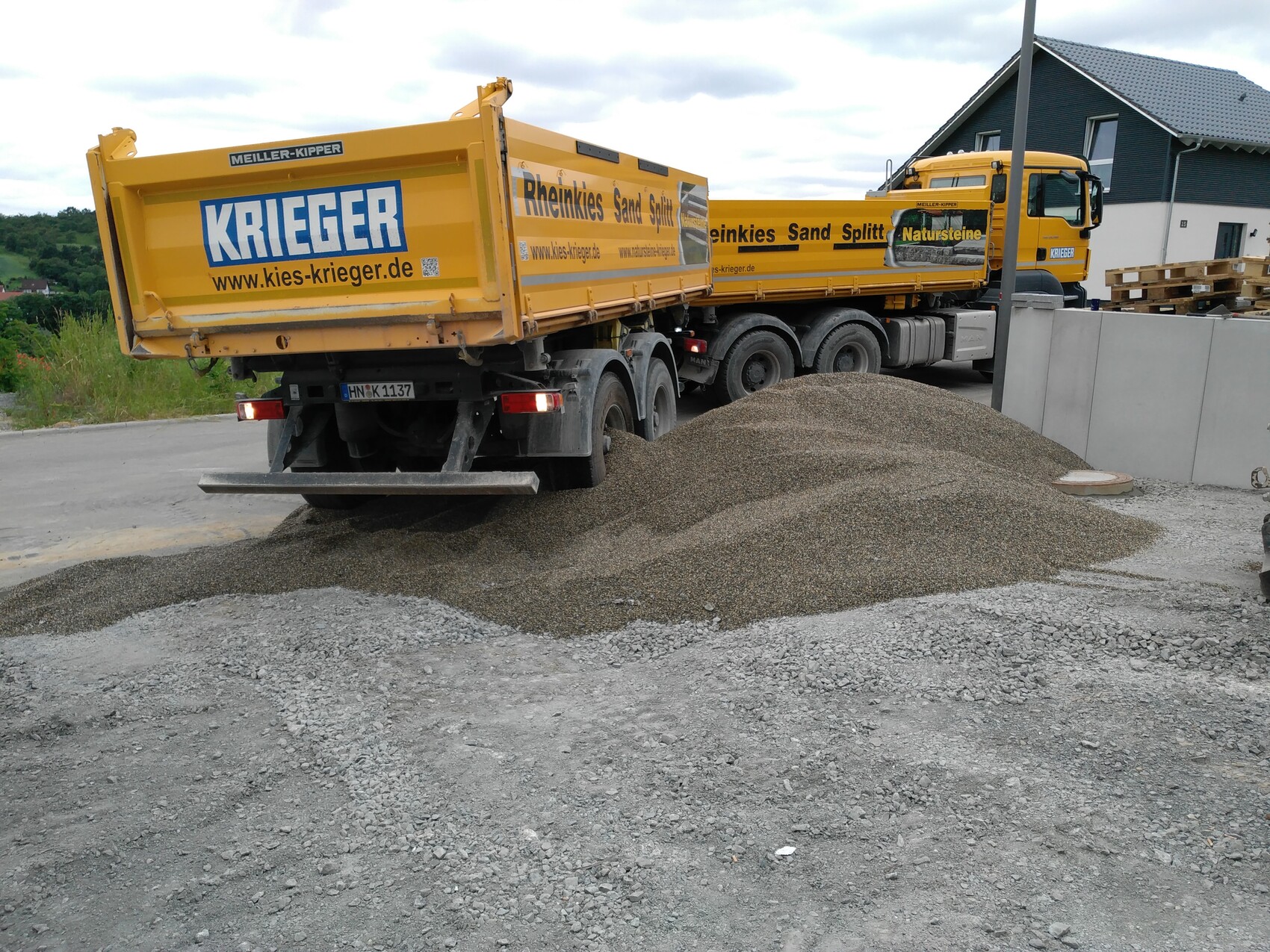Zwei gelbe Kipper-LKWs stehen auf einer Baustelle neben einem großen Kieshaufen.