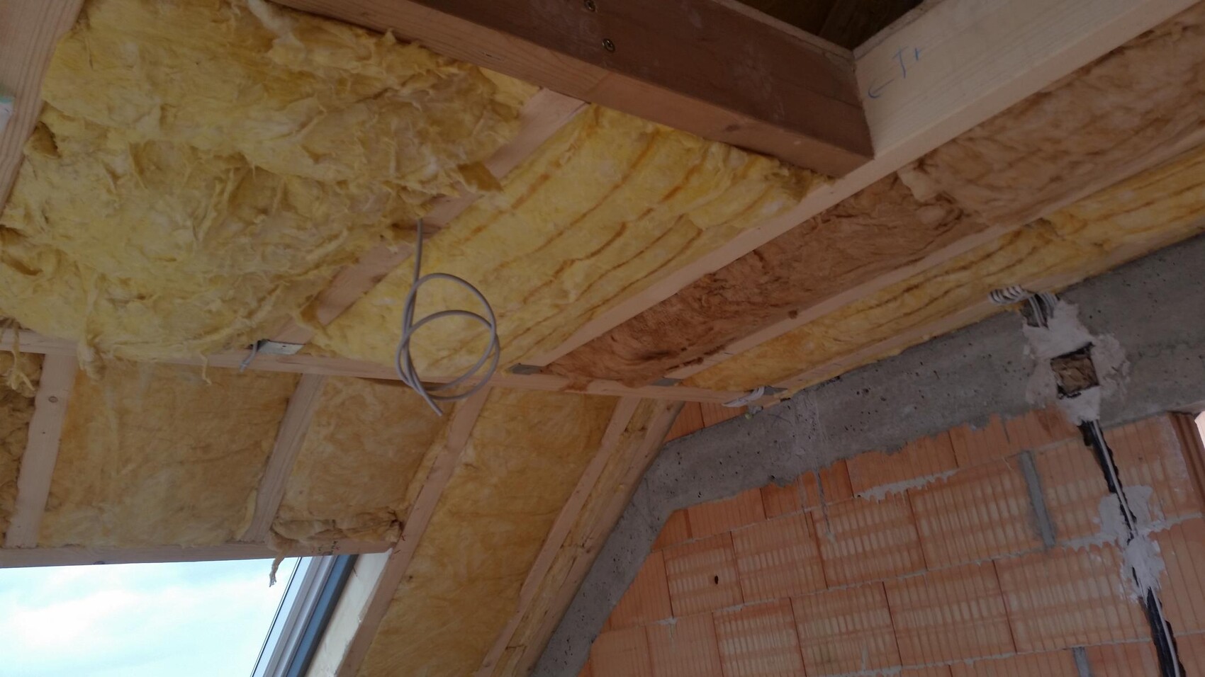Dachgeschoss mit gelber Dämmung, Holzbalken und Rohbaustrukturen im Bau