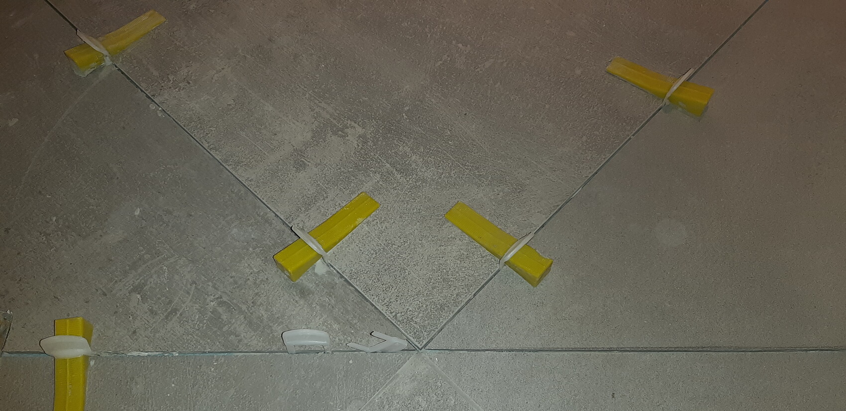 Bodenfliesenverlegung mit gelben Abstandshaltern zwischen Fliesen und weißen Clips.