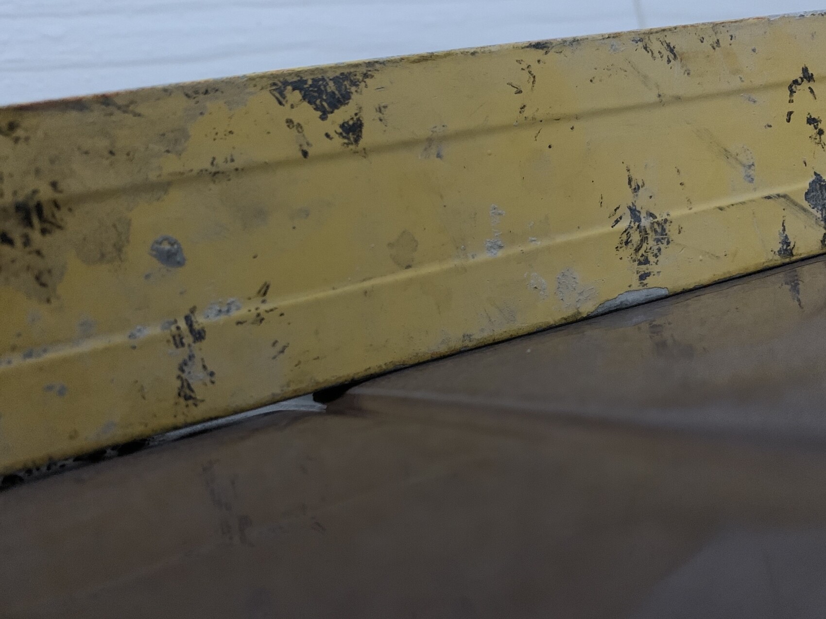 Nahaufnahme einer gelben Metallkante mit abgeplatzter Farbe und Flecken auf dem Boden.
