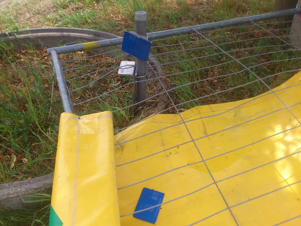 Gelbe Baustellenbarriere mit Metallzaun auf einem Baugrundstück im Gras