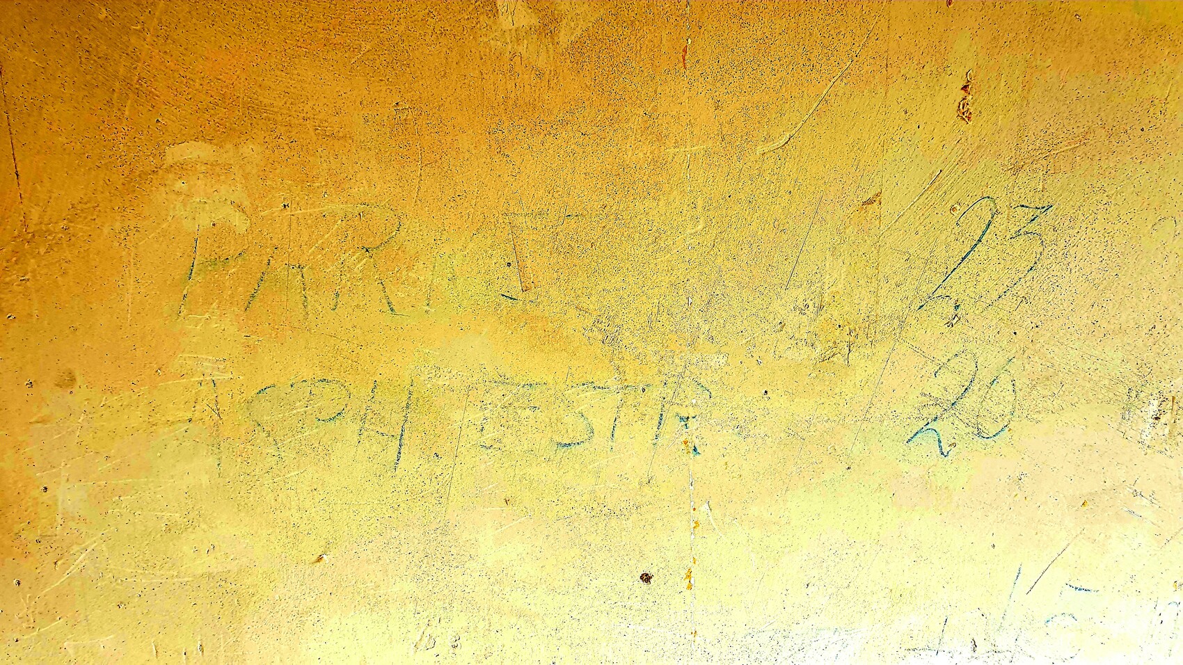 Gelbe, rauhe Wand mit Kratzspuren und blauer Graffiti-Schrift, unscharf lesbar.