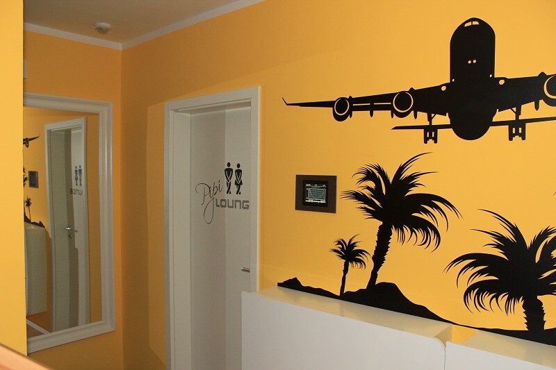 Gelber Innenraum mit Flugzeug-Wandgrafik und Palmen; Tür mit Pub Lounge.