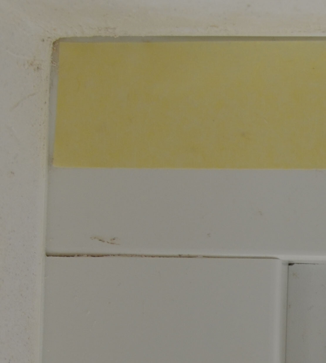 Nahaufnahme einer Badezimmerwand mit gelber Fliesenverkleidung und weißen Fliesen.
