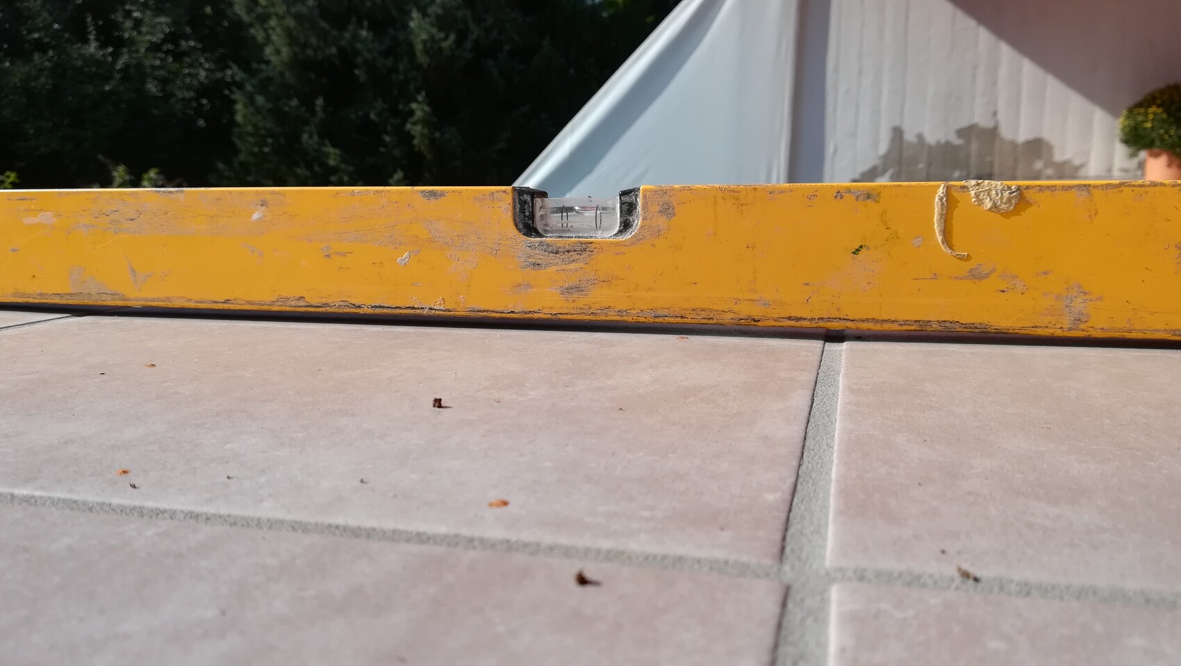 Gelbe Wasserwaage ruht auf rechteckigen Bodenfliesen einer Baustelle