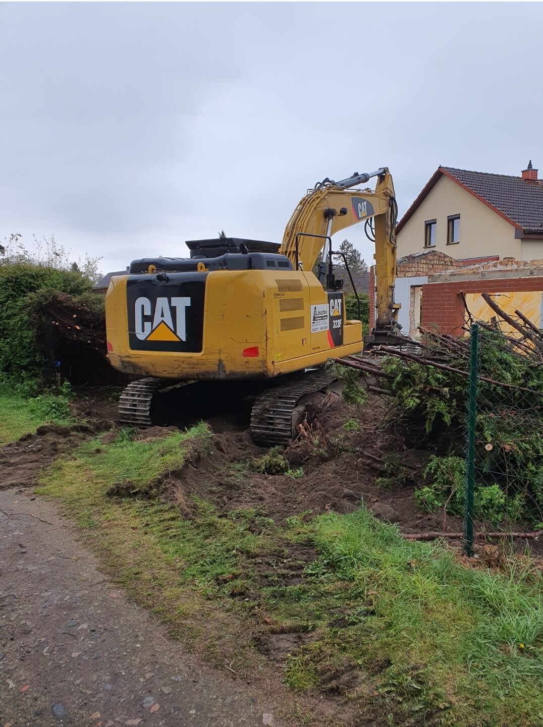 Gelber CAT-Bagger auf Baustelle neben Haus, Holzbündel und Äste im Vordergrund.