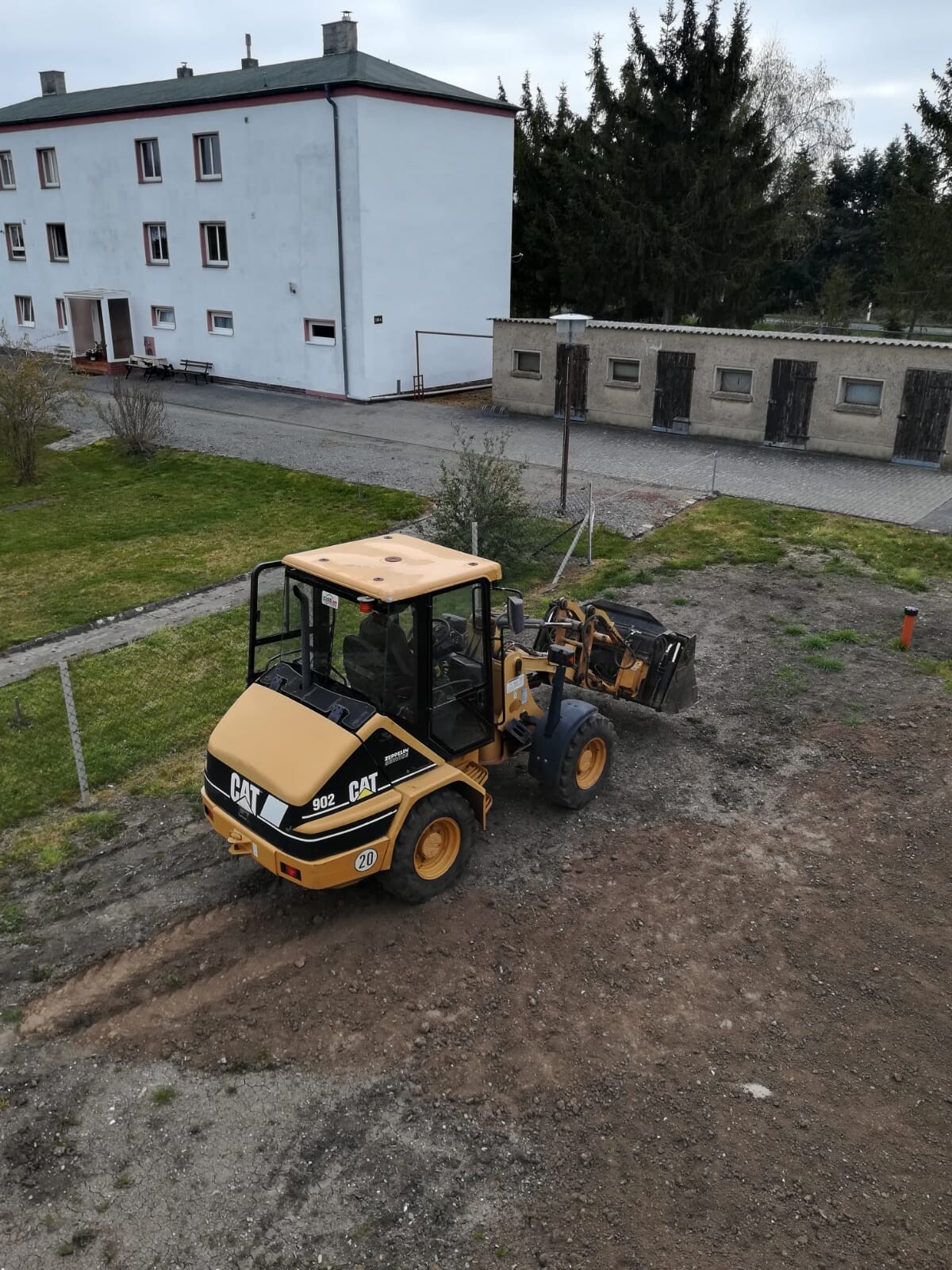Gelber CAT-Baumaschine mit Schaufel auf Kies, Gebäude im Hintergrund.