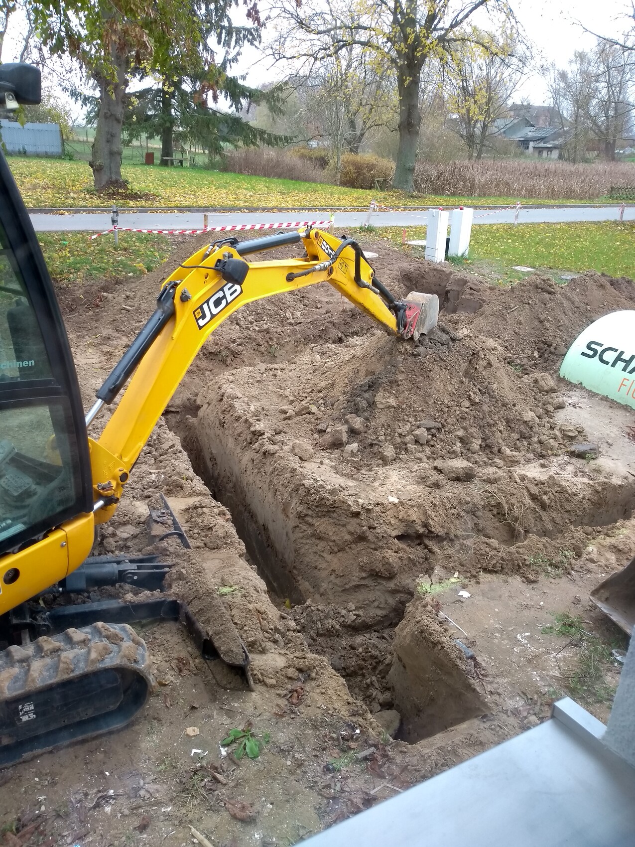 Kleiner gelber JCB-Minibagger gräbt eine Grube auf einer Baustelle, Erdhaufen daneben.