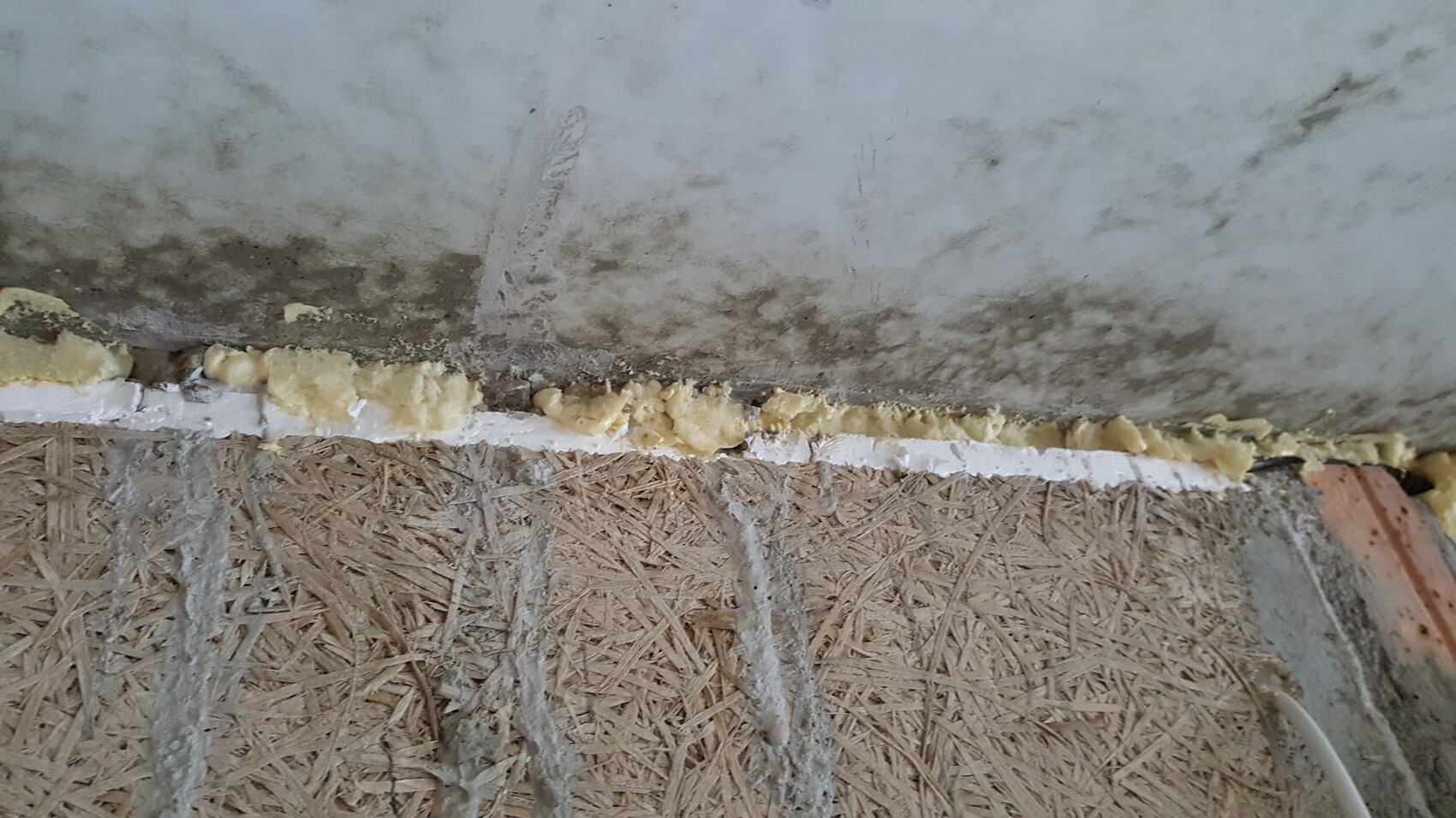 Gelber Bauschaum-Dichtstoff entlang Wand-Boden-Fuge, OSB-Untergrund sichtbar.