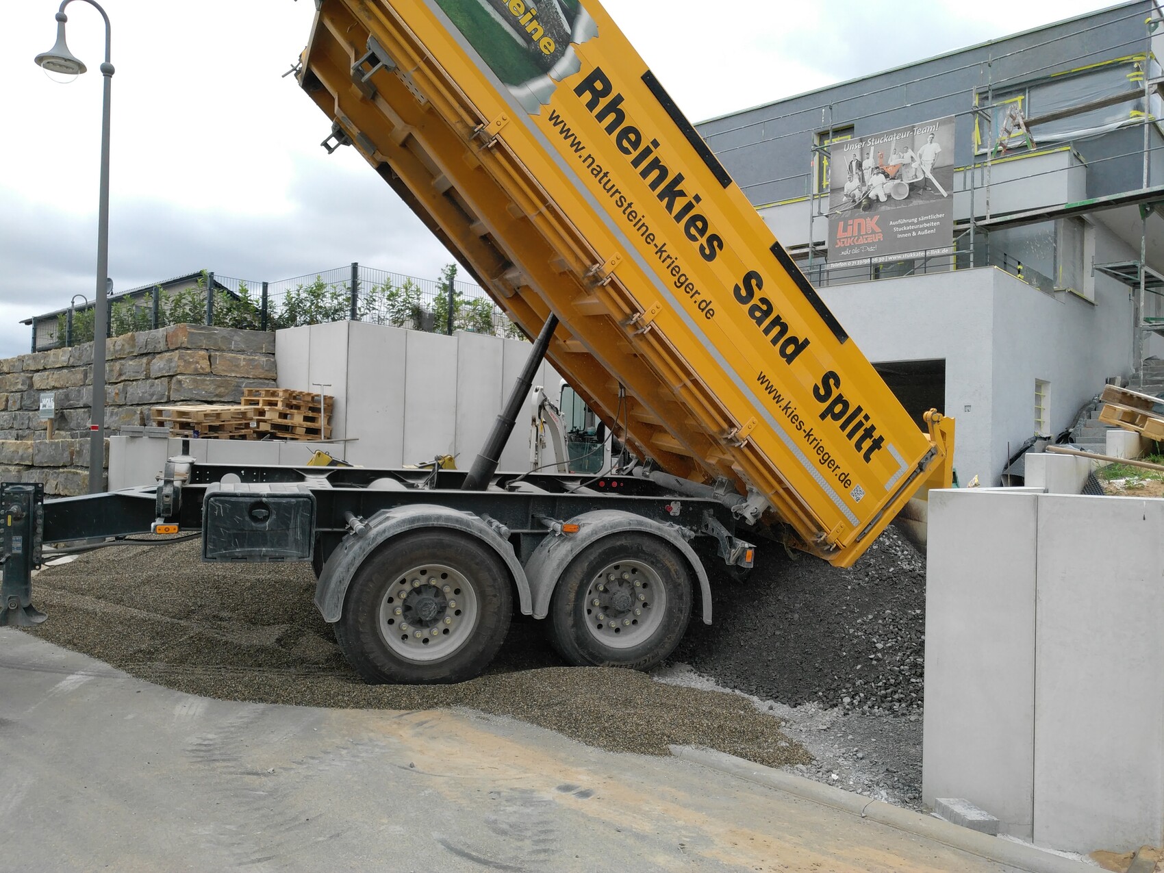Großer gelber Kippwagen kippt Sand auf einer Baustelle vor einem Gebäude.