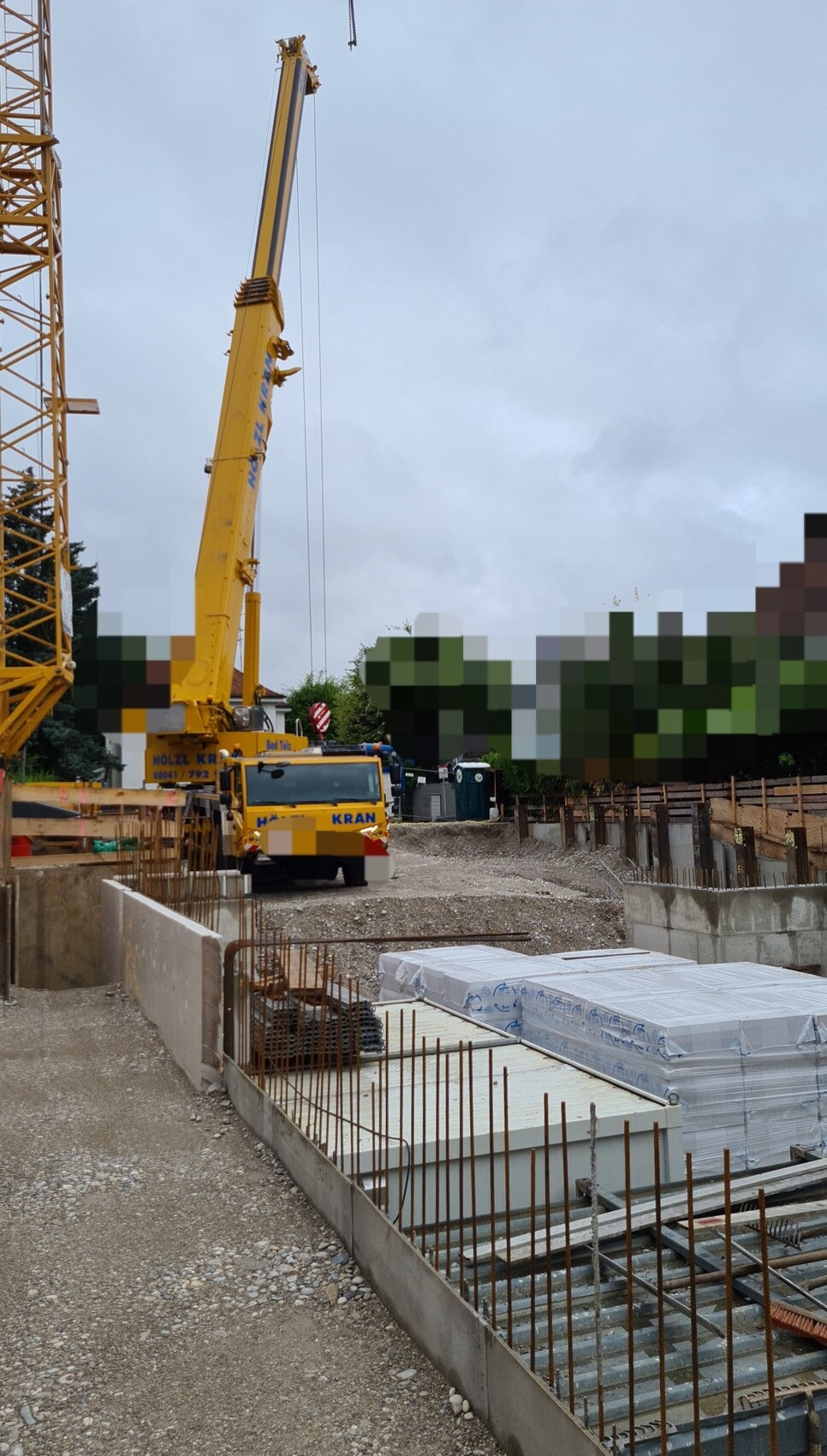 Großer gelber Baukran auf einer Baustelle mit Fundamenten, Bewehrung und Bauplatten.