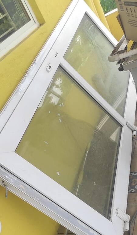 Weiße Glasfront mit Rahmen vor gelber Außenwand, leicht schräg montiert